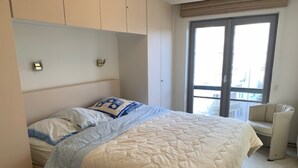 A bedroom with a bed, a chair, a window, and a door. - Apartment in Belgium With Side Sea View (Knokke-Heist)
