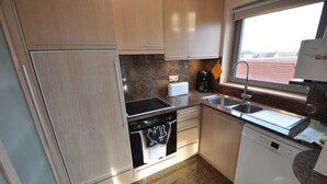 A compact kitchen with a built-in oven, dishwasher, and a window providing a view of the outside. - Apartment in Belgium With Side Sea View (Knokke-Heist)