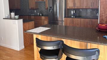 A modern kitchen with wooden cabinets, a stainless steel refrigerator, and two black bar stools.