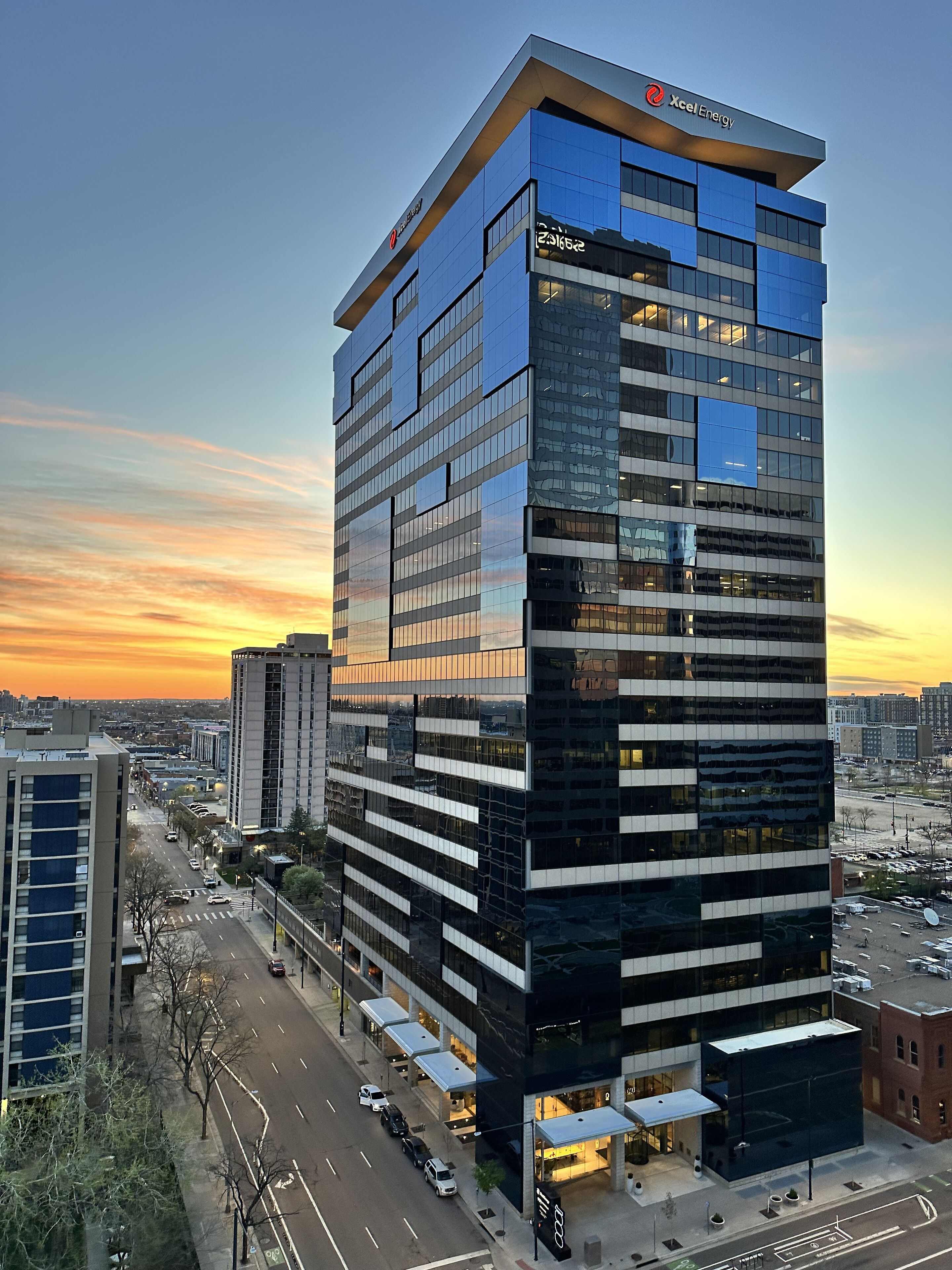 Un edificio de oficinas moderno con fachada de vidrio, un logotipo corporativo destacado y vistas del área urbana circundante.