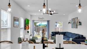 A modern kitchen with a white countertop, a black faucet, and a dining area with wicker chairs and a blue sofa. - Luxury Beach Home Sauna Cold Plunge E-bikes (Jacksonville Beach)