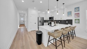 A modern kitchen with white cabinetry, a central island with bar stools, a stainless steel refrigerator, and a black and white backsplash. - Luxury Beach Home Sauna Cold Plunge E-bikes (Jacksonville Beach)