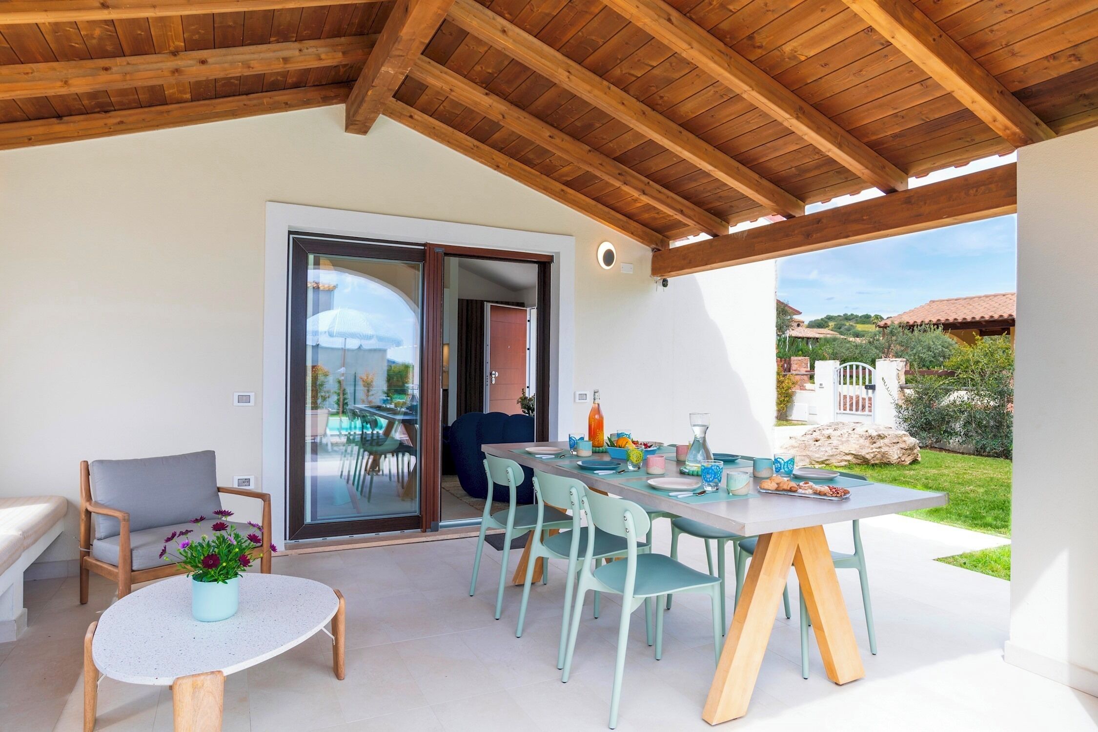 Een overdekt terras met houten plafond, een tafel gedekt voor vier personen, en uitzicht op de tuin.