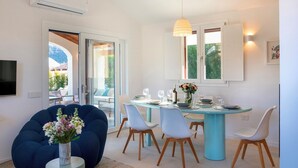 A modern dining area with a round table, white chairs, and a blue table base. - Casa Moros 6, Emma Villas (Castiadas)