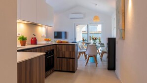 A modern kitchen with wooden cabinets, a built-in oven, and a dining area with a table and chairs. - Casa Moros 6, Emma Villas (Castiadas)