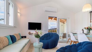 A modern living room with a sofa, blue bean bag chairs, a flat-screen TV, and a dining area with a table and chairs. - Casa Moros 6, Emma Villas (Castiadas)