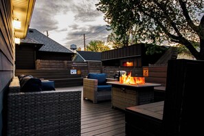 An outdoor patio with wicker furniture, a fire feature, and a wooden deck. - Downtown Indy • Walk to Stadiums • 4BR/3BA • Hot Tub • Game Room • Sleeps 13 (Indianapolis)