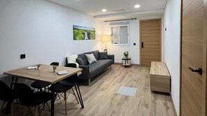 A modern living room with a wooden dining table, black chairs, a grey sofa, and a small side table with a lamp. - Apartamento moderno cerca del aeropuerto Tenerife Norte y La Laguna. (CN)