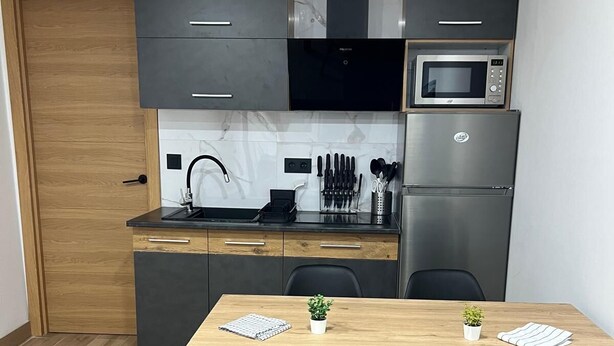 A compact kitchen with modern appliances, a wooden dining table, and black chairs. - Apartamento moderno cerca del aeropuerto Tenerife Norte y La Laguna. (CN)
