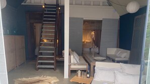 Ein modernes Interieur mit Treppe, einer Couch, einem Tisch mit Gläsern und Flaschen sowie Blick ins Freie.