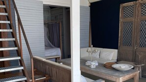 Ein Zimmer mit einer Holztreppe, einem Himmelbett, einem Esstisch mit Stühlen und einem großen Fenster.