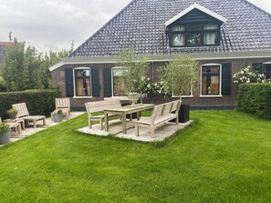 A house with a tiled roof, a brick exterior, and a well-maintained lawn with outdoor furniture.