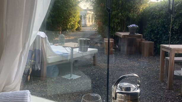 Ein gemütlicher Sitzbereich im Freien mit Tisch, Stühlen und Blick auf einen Garten.