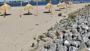 Ein Strand mit reetgedeckten Sonnenschirmen und einer felsigen Küstenlinie.