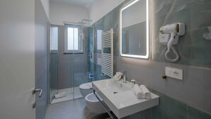Een moderne badkamer met een douchecabine van glas, een losstaand wastafelmeubel, een grote spiegel met ingebouwde verlichting en een aan de muur bevestigde haardroger.