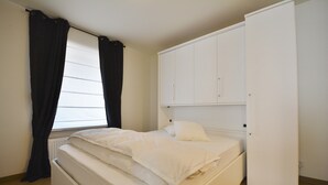 A bedroom with a bed, white wardrobe, and a window with curtains. - Apartment in Knokke Near the Beach (Knokke-Heist)
