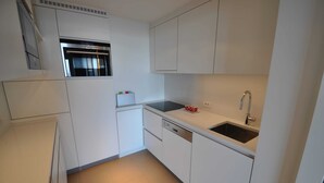 A compact kitchen with white cabinetry, a built-in oven, a dishwasher, and a sink with a faucet. - Apartment in Duinbergen by Sailing Club (Knokke-Heist)