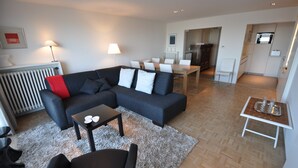 A modern living room with a sectional sofa, a dining table, and a kitchen area in the background. - Apartment in Duinbergen by Sailing Club (Knokke-Heist)