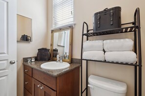 Compact bathroom with a granite sink, wooden vanity, and a shelf for essentials.