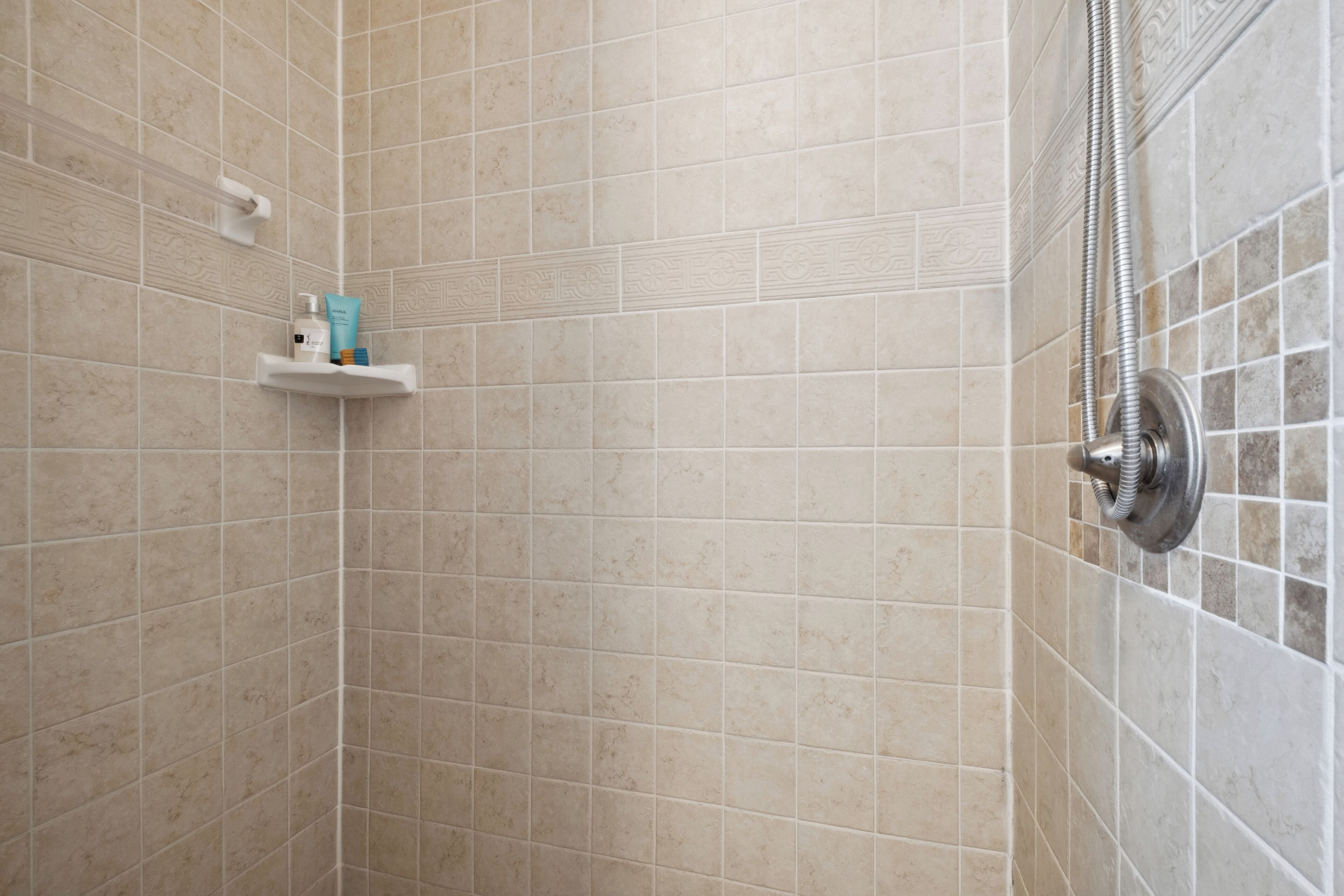 A tiled shower area with a handheld showerhead and a shelf with toiletries.