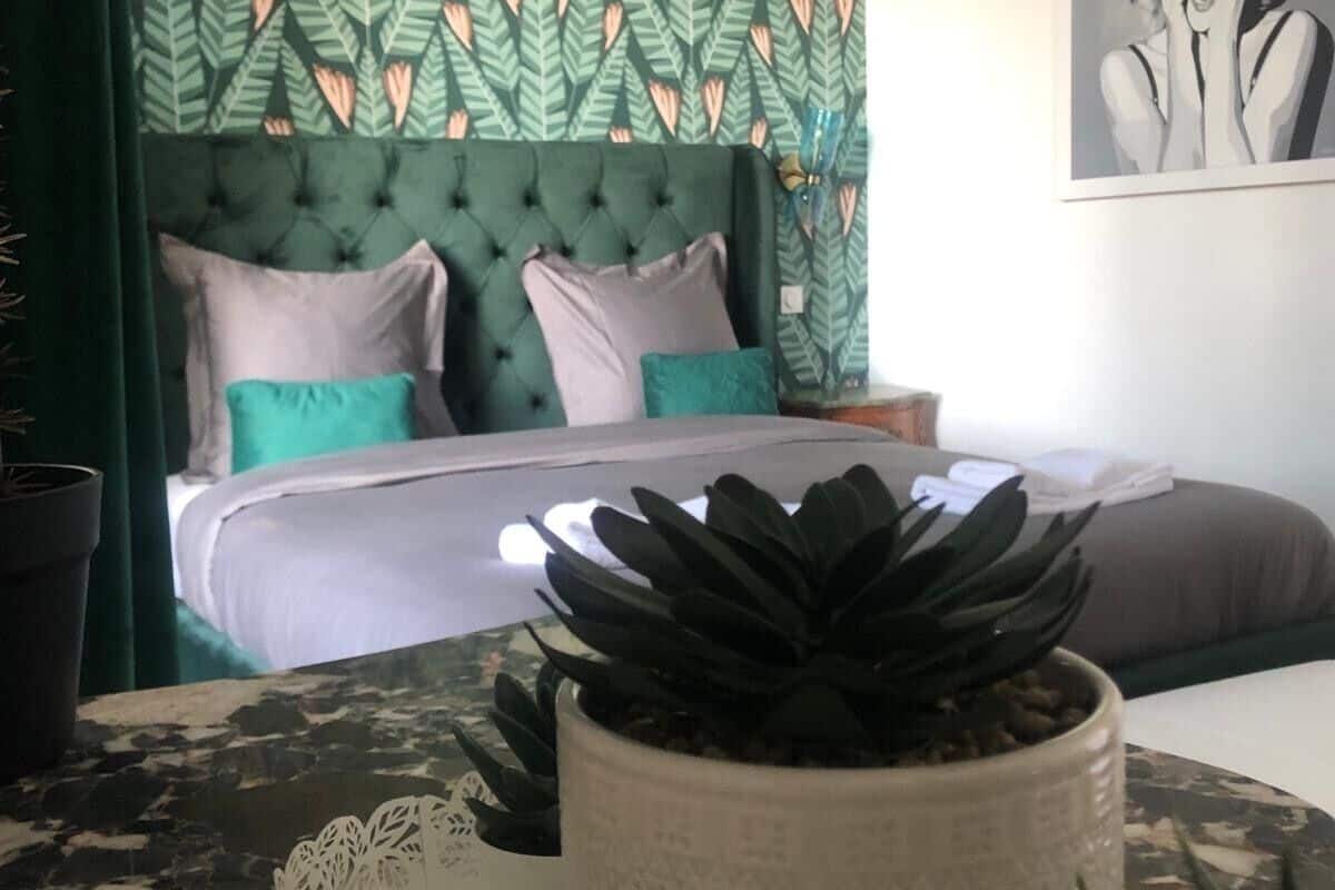 Ein Schlafzimmer mit einem grün gemusterten Kopfteil, einem Bett mit vielen Kissen und einem Blumentopf auf einem Nachttisch.
