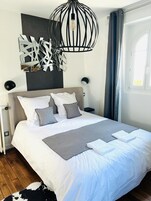 Quarto moderno com uma cama grande, uma obra de arte geométrica na parede, luminária pendente e uma janela com cortinas.