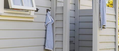 A small outdoor shower area with a window and a potted plant.