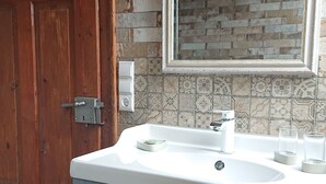 Un baño con puerta de madera, un lavamanos blanco con dos grifos y salpicadero de azulejos.