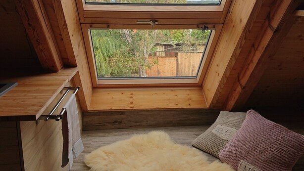 Una habitación con tragaluz, vigas de madera, alfombra de piel y un cojín tejido.