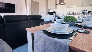 A modern living room with a black sofa, a wooden dining table set for two, and a kitchen in the background. - The Hop Store, HU1. Experience city living in a converted brewery. (Kingston upon Hull)