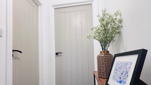 A hallway with a white door, a vase with flowers, and a framed picture on a wooden table. - The Hop Store, HU1. Experience city living in a converted brewery. (Kingston upon Hull)