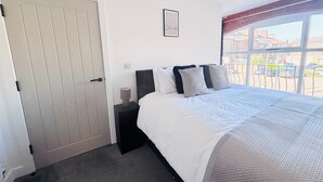 A bedroom with a bed, a nightstand, a door, and a window with a view of buildings and cars outside. - The Hop Store, HU1. Experience city living in a converted brewery. (Kingston upon Hull)