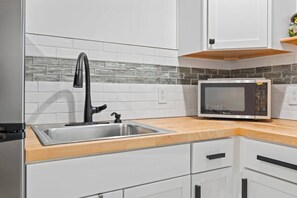 A kitchen with a stainless steel sink, a modern faucet, a microwave, and white cabinets.