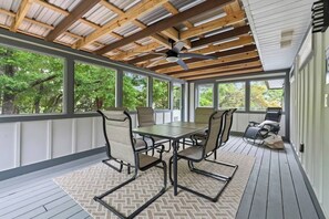 A covered patio with a table and chairs, large windows, and a ceiling fan.