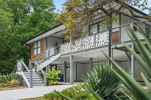 A modern two-story building with a covered outdoor area, a staircase, and a balcony with a railing.
