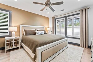 A bedroom with a bed, bedside tables, a ceiling fan, and large windows with blinds.