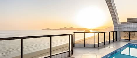 A modern hotel balcony with a view of the beach and sunset.
