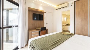 Een hotelkamer met een bed, een bureau met stoel, een televisie, een raam met gordijnen en een badkamer die door een geopende deur zichtbaar is.