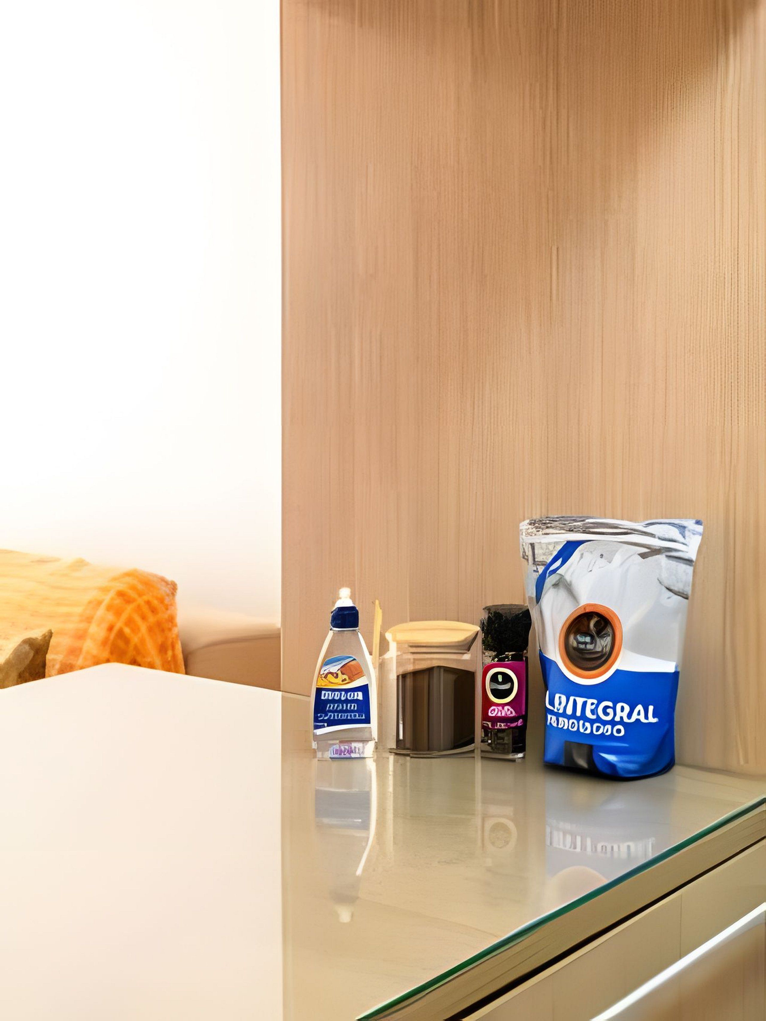 Habitación de hotel con pared de madera, una mesa de vidrio, una botella de jabón para manos, un recipiente pequeño y un paquete de papel higiénico.