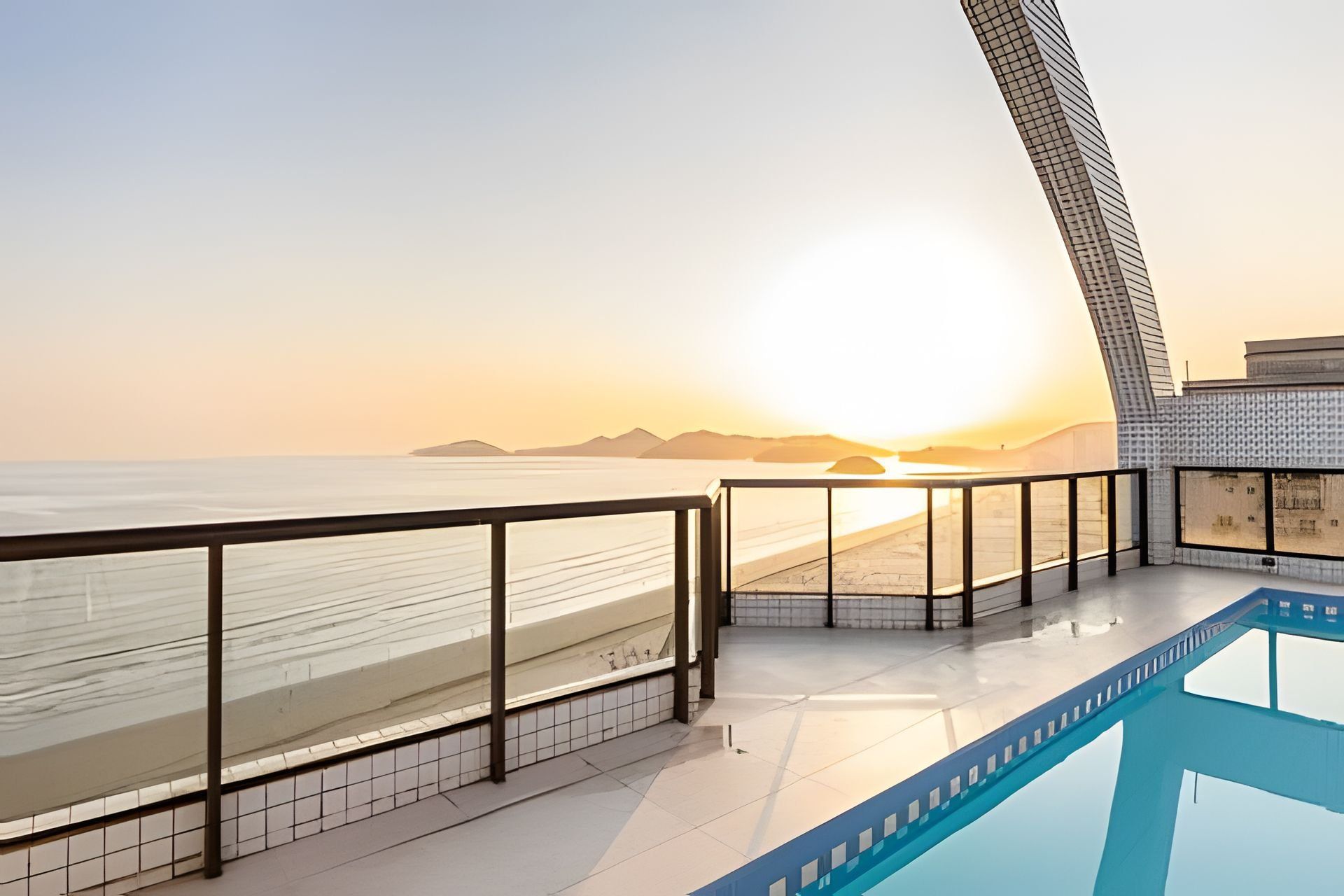 A modern hotel balcony with a view of the beach and sunset.