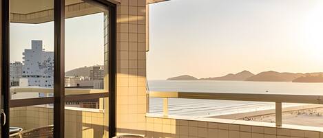 A balcony with a view of the sea and mountains, a table with plates and glasses, and a chair.