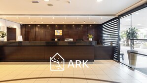 Een receptiebalie met een donker houten afwerking, erboven een lijst met foto en een logo met een icoontje van een huis en de tekst 'ARK'.