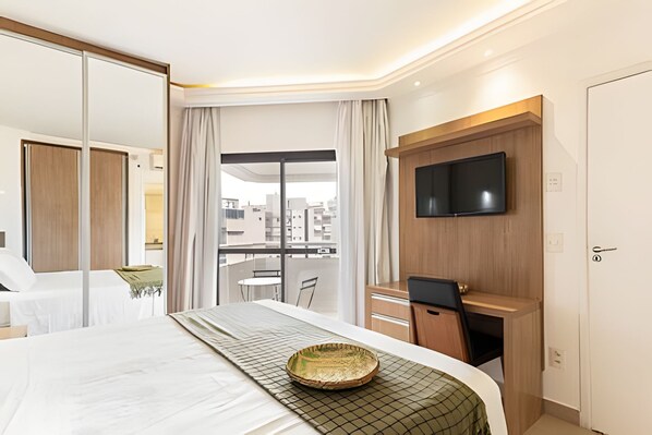 Une chambre d’hôtel équipée d’un lit, d’un bureau, d’une télévision et offrant une vue sur le paysage urbain.