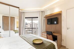 Habitación de hotel con cama, escritorio, televisor y vista a la ciudad.