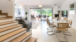 Una sala de estar moderna con una escalera, un comedor con sillas de mimbre y un televisor montado en la pared.