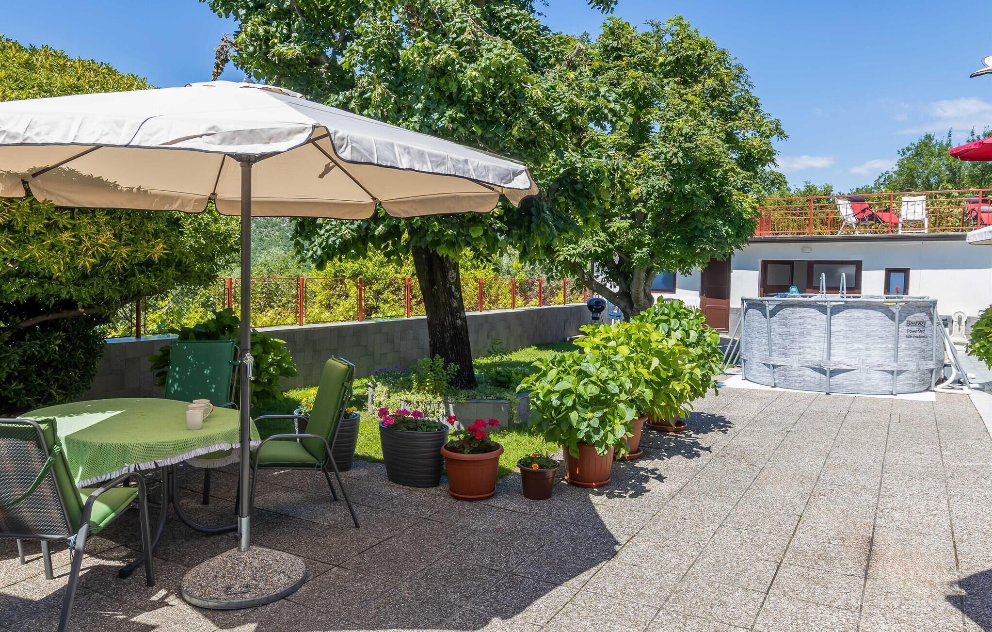 An outdoor patio area with a table and chairs under a canopy, surrounded by potted plants and a swimming pool.