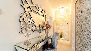 A hallway with a decorative mirror, a glass console table with a candelabra, a patterned armchair, and a potted plant. - Cozy apartment in Sali with WiFi (Sali)