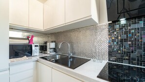 A modern kitchen with white cabinets, a black sink, and a backsplash with mosaic tiles. - Cozy apartment in Sali with WiFi (Sali)