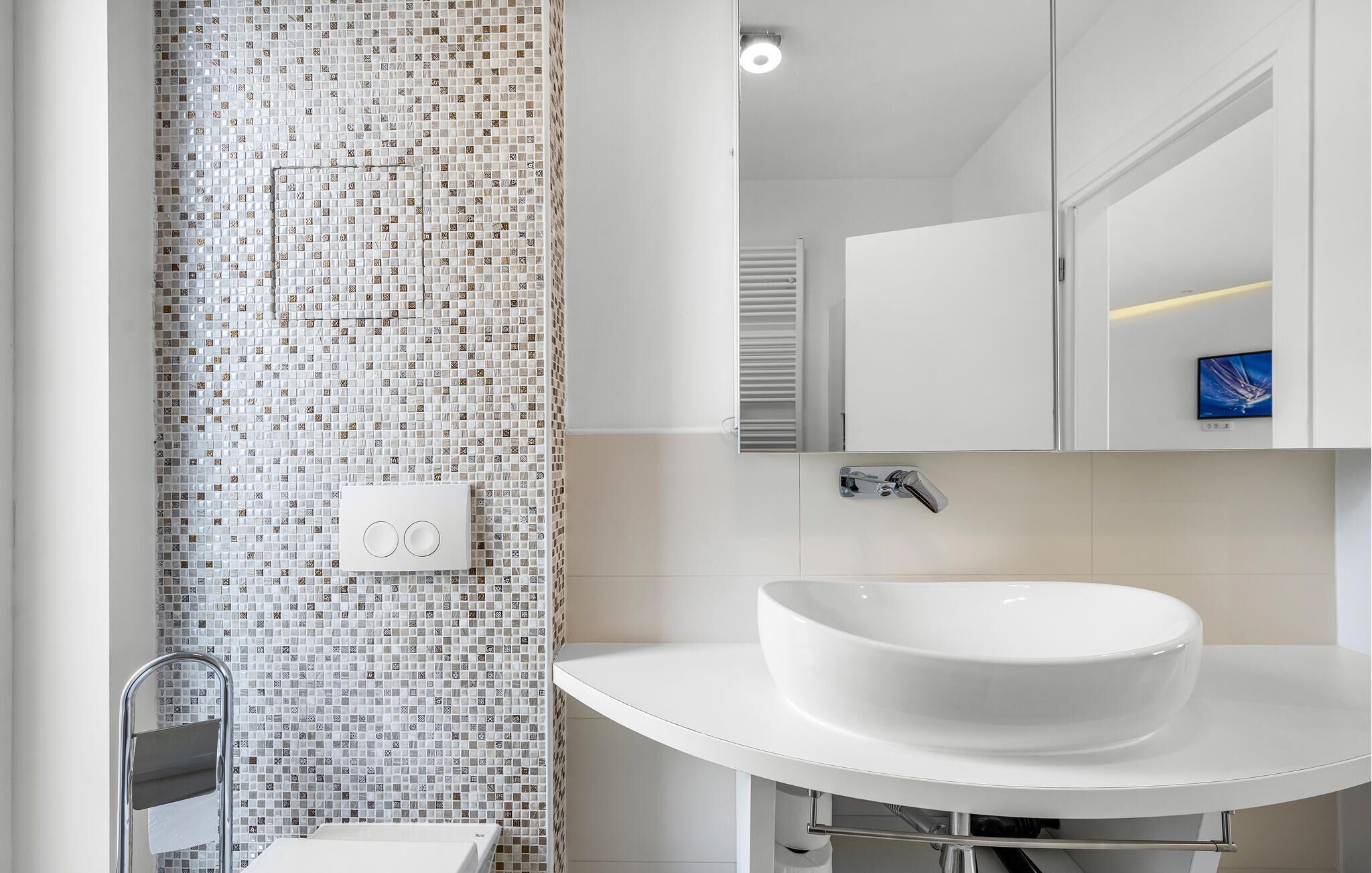 A modern bathroom with a mosaic tile wall, a white sink, and a mirror above it.