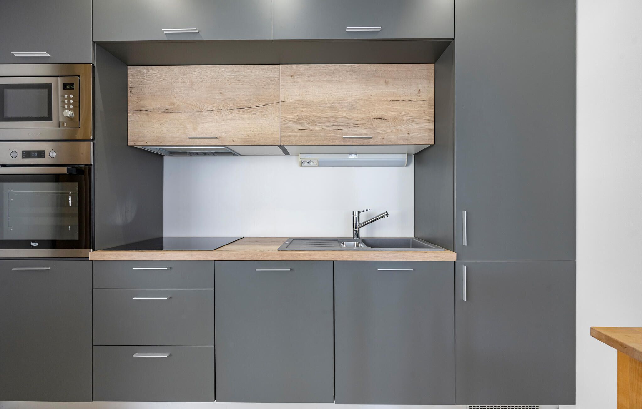 A modern kitchen with grey cabinets, a wooden countertop, a built-in microwave, and a stainless steel oven.